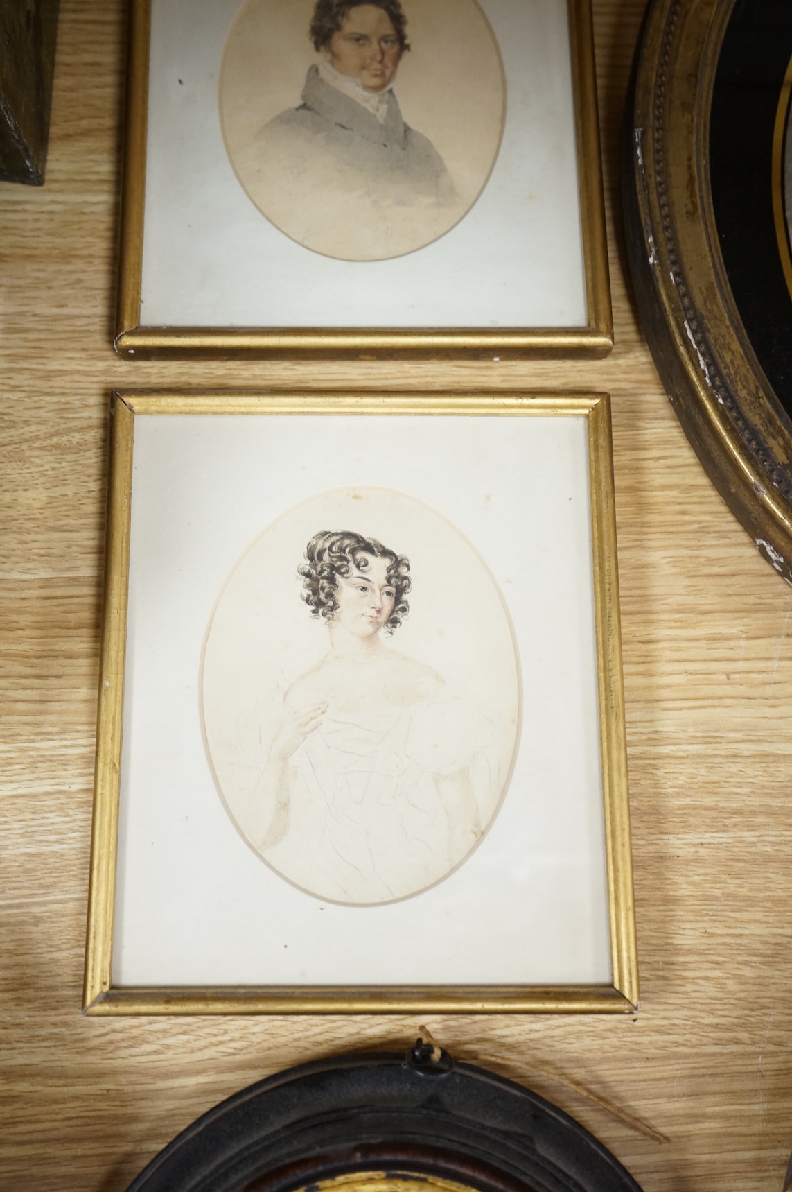Four Regency and early Victorian portraits to include a pair of a lady and gentleman together with a carved wax bust of a lady wearing a bonnet, housed in an ebonised and gilt oval box frame, largest overall 38 x 32cm